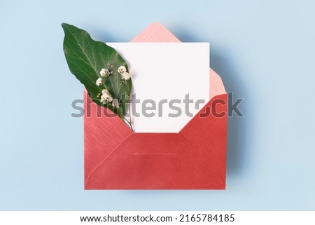 Open envelope with flowers and white blank card on light blue background, copy space, top view