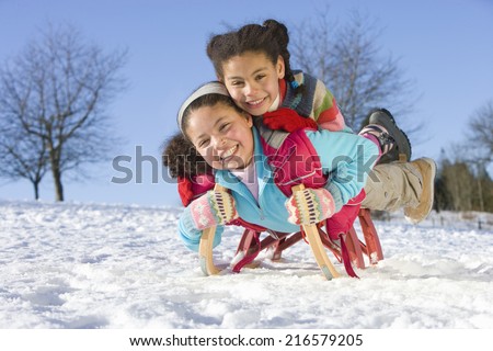 Excited girls sledding down snowy hill on sled