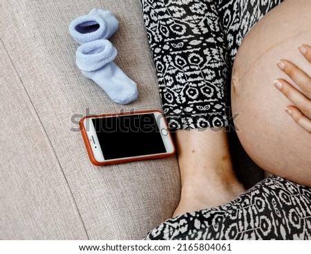Pregnant expectant viewing pictures online via social networks relaxing on bed with mobile smart phone. Pregnant woman with smart phone.