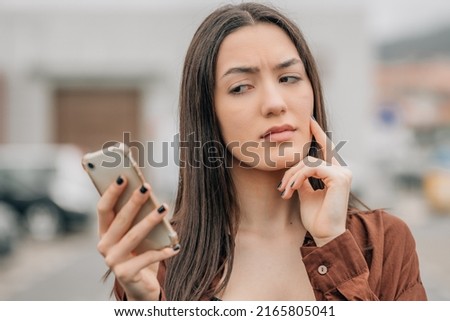 girl looking at the mobile phone pensive with mistrust Royalty-Free Stock Photo #2165805041