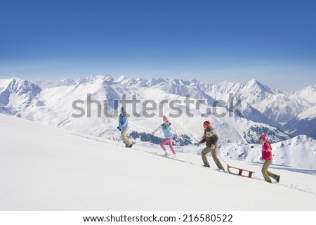 Family pulling sled uphill with mountains in background