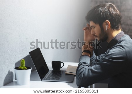 Side portrait of young thoughtful man with closed eyes working online at home.