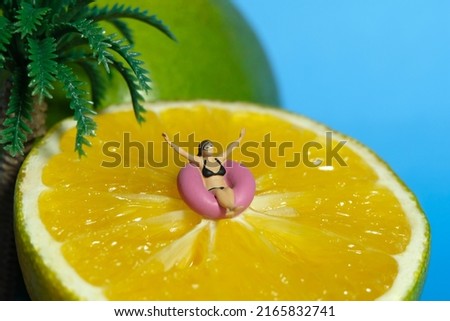 Miniature people toy figure photography. Girl wearing black sunglass swimming with rubber tube ring above slice orange fruit. Tropical island with palm coconut tree concept. Image photo