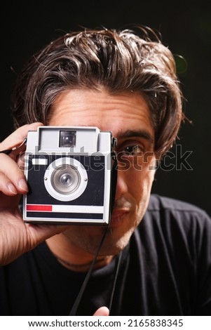 young man taking a picture with an antique camera. with black t-shirt and black background.