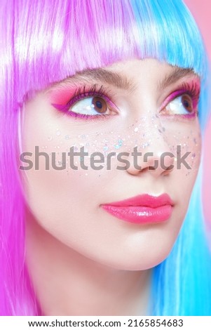 Anime makeup. Pretty girl with bright makeup, glitter freckles and in colored violet-blue wig. Pink background. Hairstyle, hair coloring, make-up. Japanese anime style. 