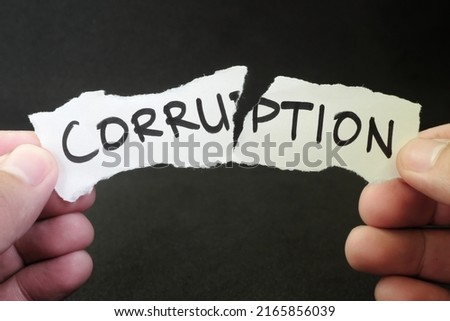 Stop and fight corruption concept. Human hand tearing a piece paper with written word corruption. Royalty-Free Stock Photo #2165856039
