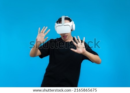 Asian man in black t-shirt wearing vr headset posing playing and touching on the blue screen background.
