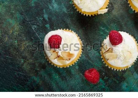 Light delicious dessert - muffins with cream, fresh raspberries and almond flakes. Isolated on a dark green background. View from above. Birthday, anniversary, romantic date.