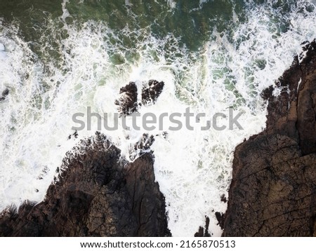 View from above. Storm in the ocean. White foamy waves crash against large boulders on the shore. The greatness and beauty of nature, ecology, environmental protection, geology.