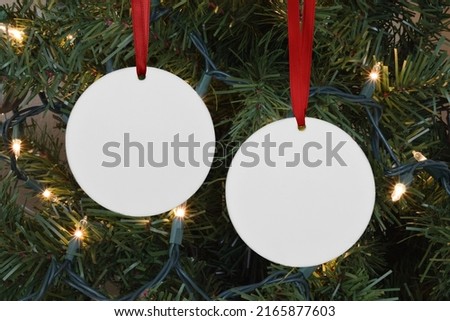 Closeup of two round Christmas Ornaments hanging merrily from a lit up Christmas tree. Royalty-Free Stock Photo #2165877603