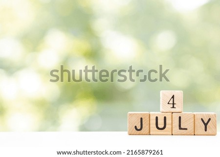 July 4, Date design with calendar cube on wooden table and green background.