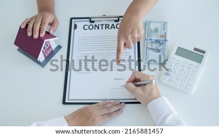 A real estate agent with a house model is talking to clients about buying home insurance and having customers sign contracts under the formal contract agreement. Home rental and insurance concept.