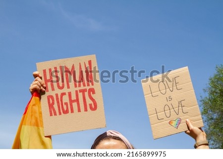 Protesters holding placard signs Human Rights and Love is Love with rainbow flag heart, symbol of LGBT. Pride Parade, equality march to support and celebrate LGBT+, LGBTQ gay lesbian community.