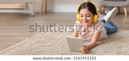 Little girl with headphones and tablet computer listening to music at home