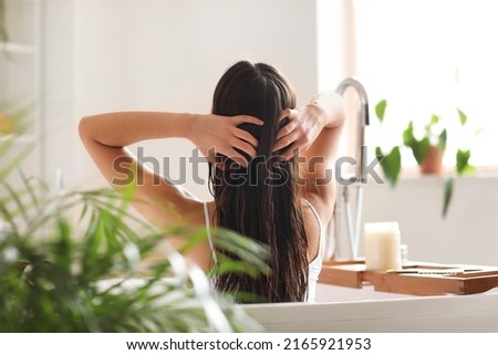 Young woman applying coconut oil onto her hair in bathroom Royalty-Free Stock Photo #2165921953
