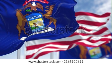 The Michigan state flag waving along with the national flag of the United States of America. In the background there is a clear sky. Michigan is a state in the upper Midwestern of United States