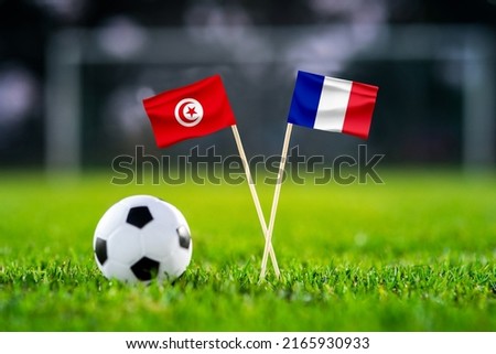 October 2022: Tunisia vs. France, Education City, Football match wallpaper, Handmade national flags and soccer ball on green grass. Football stadium in background. Black edit space. Royalty-Free Stock Photo #2165930933