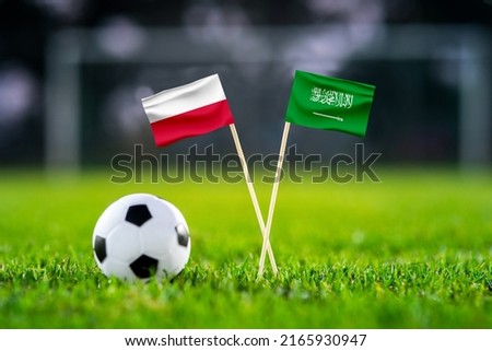 October 2022: Poland vs. Saudi Arabia, Education City, Football match wallpaper, Handmade national flags and soccer ball on green grass. Football stadium in background. Black edit space.