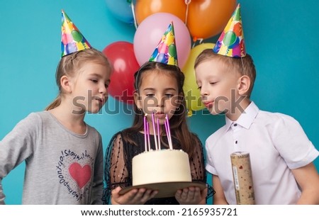 Two little girls and boy blowing candles on cake, happy birthday party.