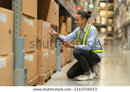 Asian man stocking worker holding tablet and checking inventory, counting the number of boxes at a wholesale store warehouse