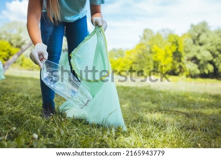 An unrecognizable woman cleans the park of garbage. Unrecognizable young volunteer collects garbage in the park.