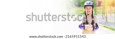 Portrait of a happy girl in a protective helmet, protective elbow pads on the background of a sports field. Rollerblading safely. Sport, leisure and protection concept. Banner. Copy space