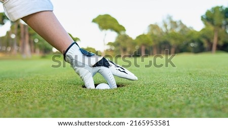 A golfer pulls a golf ball out of the hole. Ball deep