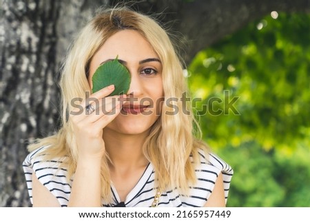 young blond Caucasian girl with a green leaf on the eye. medium closeup outdoor summer. High quality photo