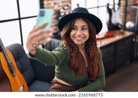 Young hispanic woman musician making selfie by the smartphone at music studio