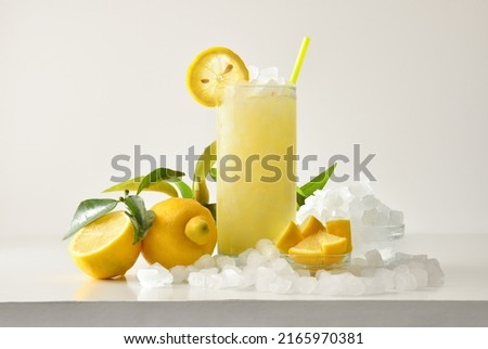 Lemon slush in tall glass with fruit and crushed ice around it on white table with isolated background. Front view. Horizontal composition. Royalty-Free Stock Photo #2165970381