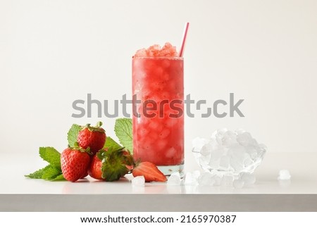 Strawberry slush drink in tall glass with fruit and crushed ice around it on white table with isolated background. Front view. Horizontal composition.