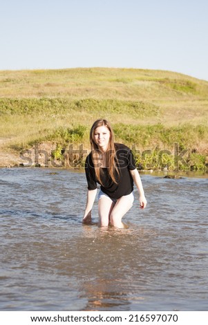 Beautiful girl with long, straight hair posing and playing with water in a small river
