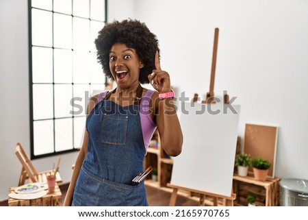Young african american woman with afro hair at art studio pointing finger up with successful idea. exited and happy. number one. 