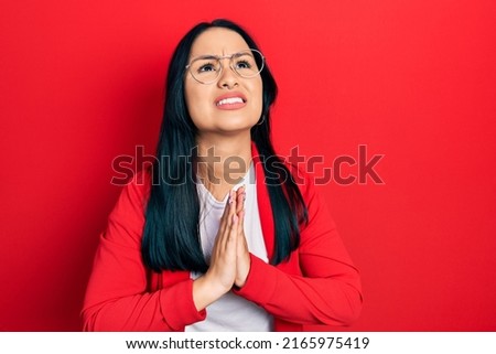 Beautiful hispanic woman with nose piercing wearing casual look and glasses begging and praying with hands together with hope expression on face very emotional and worried. begging. 