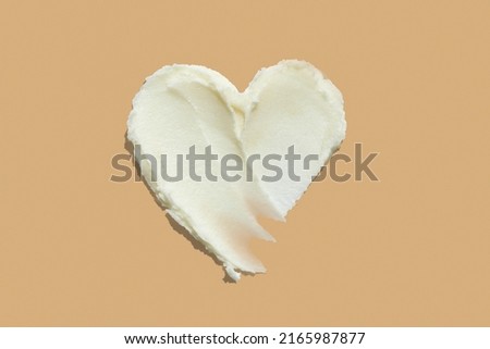 Shea butter cream textured heart shape smear on beige brown colour background, hair and skin care love swatch