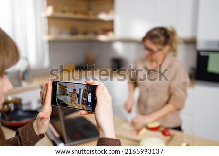 Mom and daughter recording a cooking live stream. Girl with smartphone recording video of her mother cooking