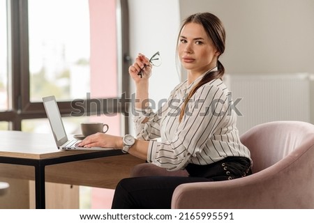 Successful business woman in shirt wearing glasses working with a laptop in the office
