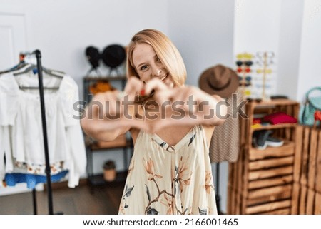Young caucasian woman at retail shop smiling in love doing heart symbol shape with hands. romantic concept. 