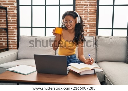 Young chinese woman listening to music studying sitting on sofa at home