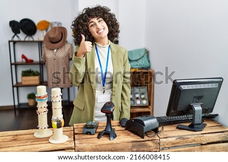 Young middle eastern woman working as manager at retail boutique doing happy thumbs up gesture with hand. approving expression looking at the camera showing success. 