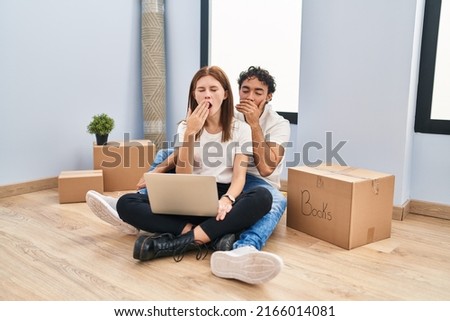 Young couple using laptop at new home bored yawning tired covering mouth with hand. restless and sleepiness. 