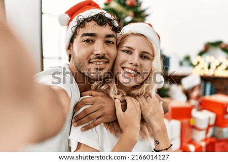Young couple smiling happy wearing christmas hat making selfie by the smartphone at home.