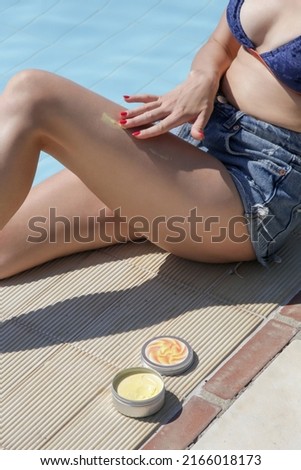 Woman on the edge of a pool applying sun cream on legs 