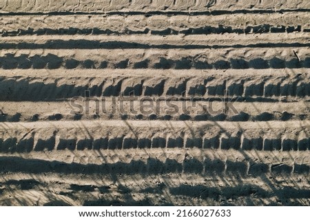Beige sand with traces of bicycle treads in the rays of the setting sun. Background with abstract texture.