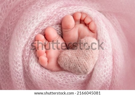 Knitted pink heart in the legs of a baby. Soft feet of a new born in a pink wool blanket. Close-up of toes, heels and feet of a newborn. Macro photography the tiny foot of a newborn baby.  Royalty-Free Stock Photo #2166045081