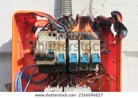 Burning switchboard from overload or short circuit on wall. Circuit breakers on fire and smoke from overheating due to poor connection. Dangerous home electrical wiring concept, closeup view Royalty-Free Stock Photo #2166046827