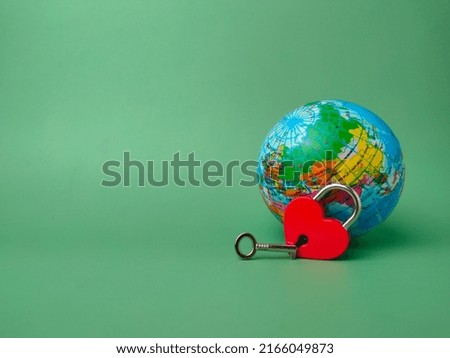 Selective focus.Heart shaped red lock with key and earth globe on a green background. Concept of love nature forever with padlock.