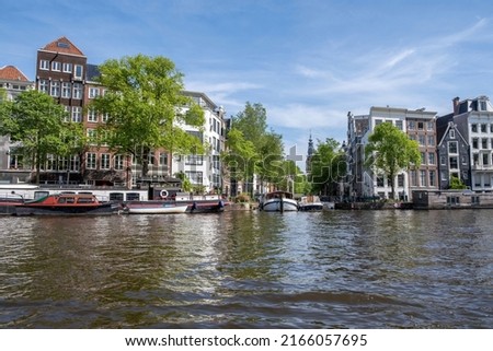 Houseboats and boats in canal, Amsterdam. Traditional brick façade houses. Blue sky, sunny day in a residential neighborhood, Netherlands.