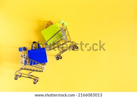 Grocery baskets with colored bags of green and blue on a yellow kopi space background.