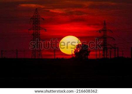 Beautiful, dramatic, colorful clouds and sky at sunset. Electrical wires and stakes and water reflexions. Image has grain texture seen at its maximum size 